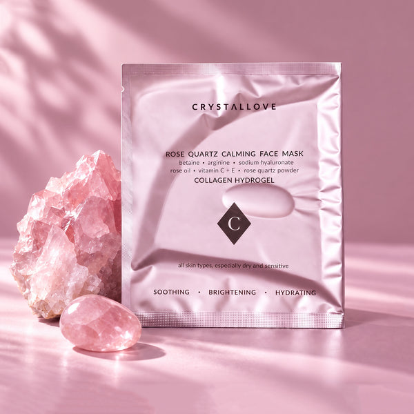 Jasnoróżowa saszetka maski do twarzy Rose Quartz Calming Face Mask marki Crystallove (maska z kwarcem różowym). Obok opakowania leży duży, surowy kryształ kwarcu różowego oraz mniejszy, wygładzony kamień. Estetyczna kompozycja na różowym tle z delikatną grą światła i cieni liści